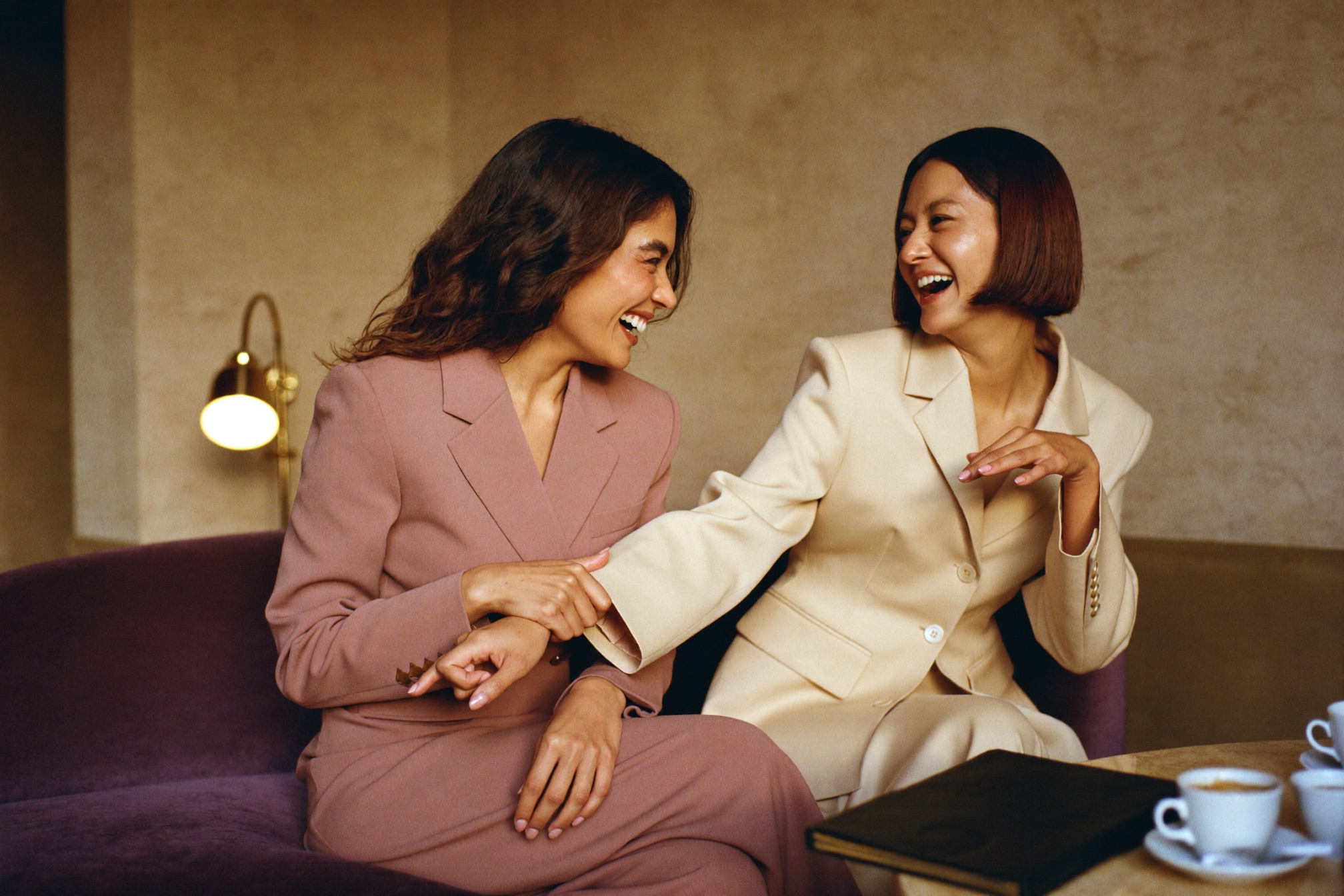Two women founders laughing together on a sofa